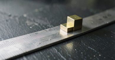 Barra de aço graduada com cursor de latão além da última marca, sob luz âmbar